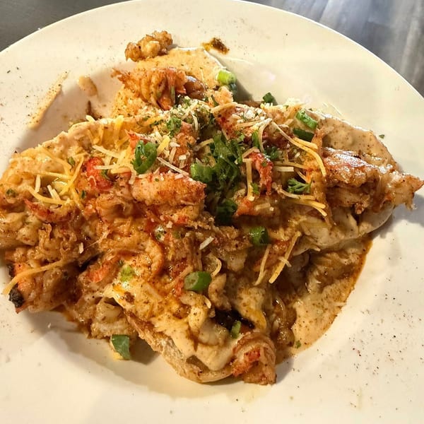Close-up of a dish with crawfish, cheese, and green onions on a white plate.