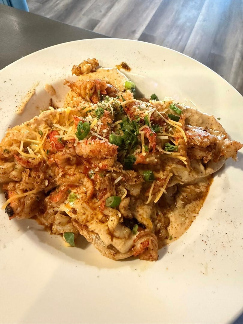 Close-up of a dish with crawfish, cheese, and green onions on a white plate.