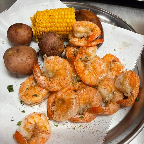 Boiled shrimp, corn on the cob, red potatoes, and sausage on a metal tray with parchment paper.