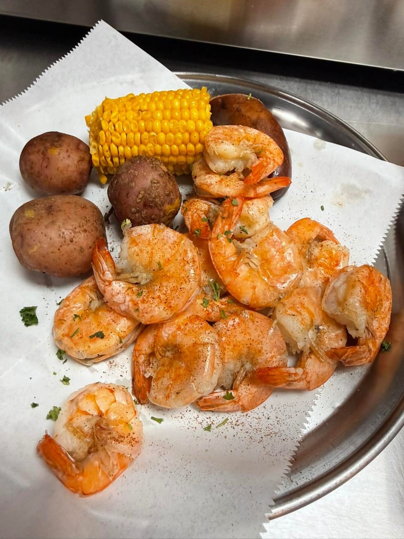 Boiled shrimp, corn on the cob, red potatoes, and sausage on a metal tray with parchment paper.