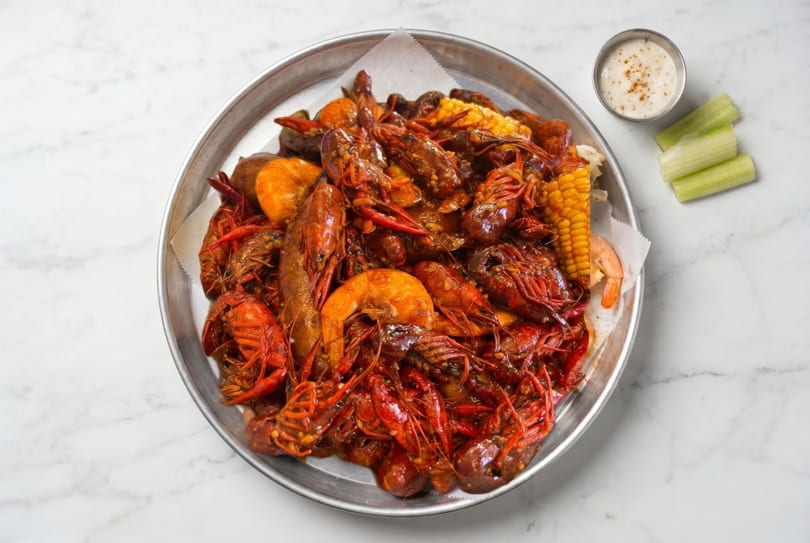 A large metal platter filled with Cajun-style crawfish, shrimp, corn on the cob, and potatoes.
