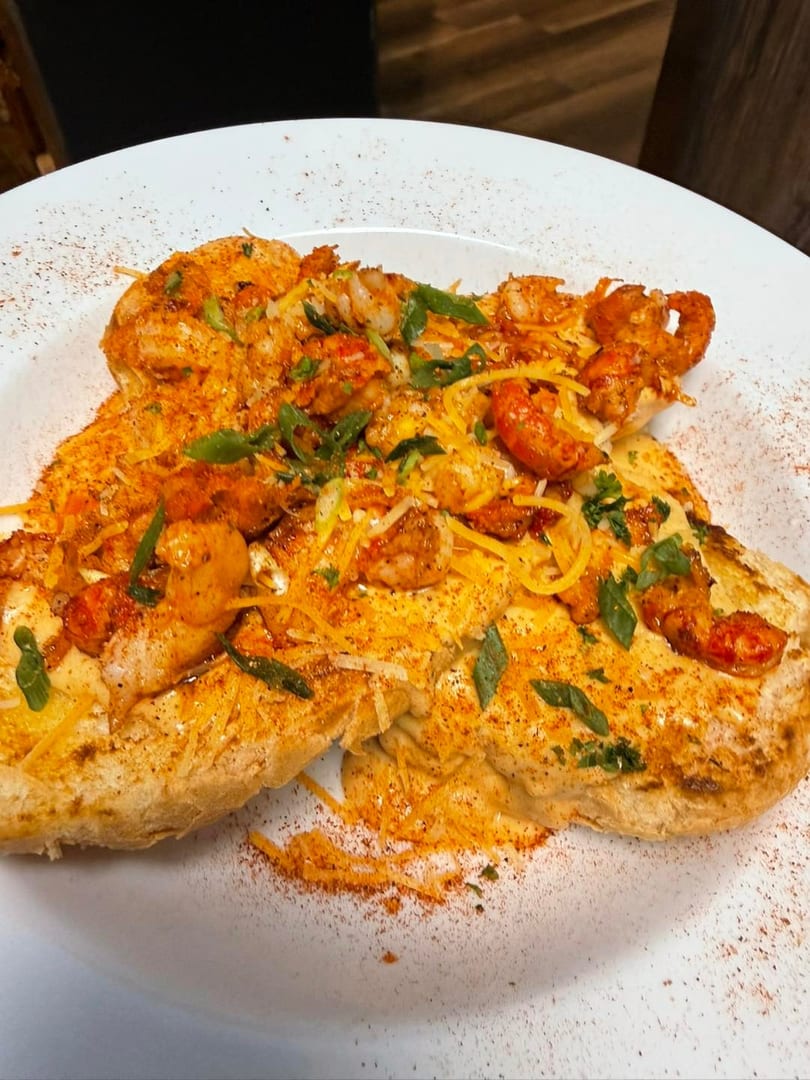Two pieces of cheesy garlic bread topped with shrimp, crawfish, and green onions.
