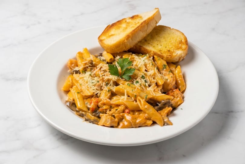 Penne pasta with creamy sauce, chicken, mushrooms, and two slices of garlic bread.