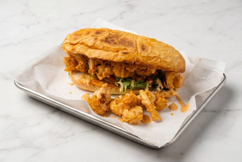 Crispy shrimp po'boy sandwich with lettuce and sauce on a metal tray with white paper.